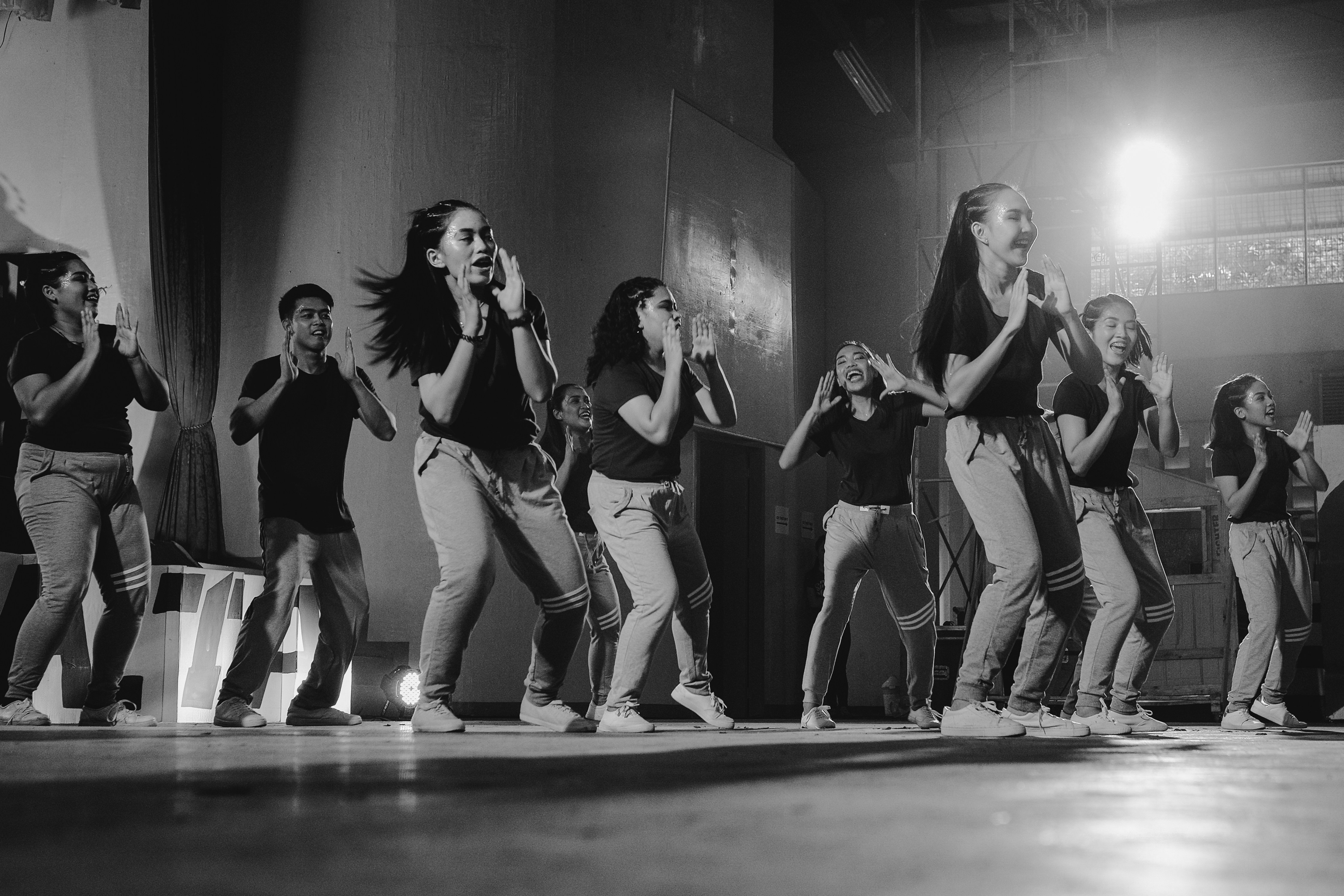 Black and white photo of teens rehearsing a dance routine on a stage.